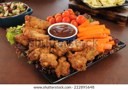 A holiday snack platter with chicken wings, carrot sticks, cherry tomatoes, salads, and chips