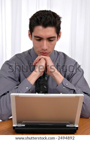 A young man in front of the office window curtains working on a laptop computer