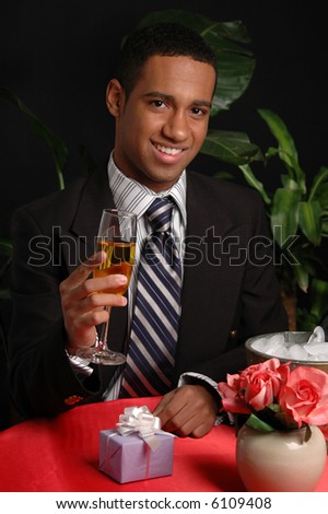 A happy young man tipping a glass of champagne to someone across the table