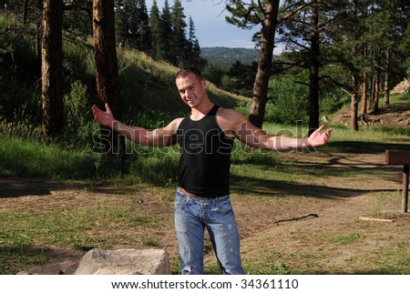 A handsome man in a campground holding his arms out wide