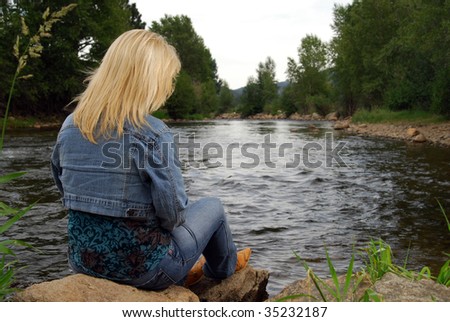 A mature woman in western wear by a mountain stream