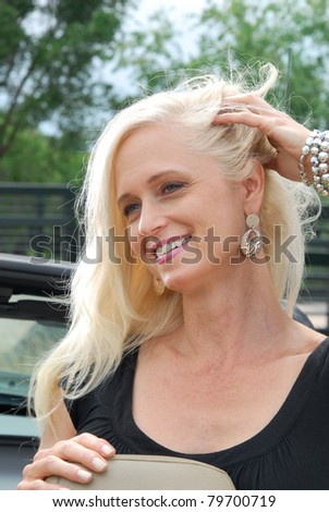 A beautiful blond woman in a car with the top down near a bridge over a stream