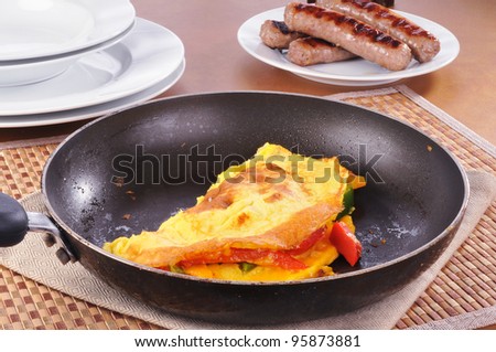 A skillet with a western omelet and a plate of sausage