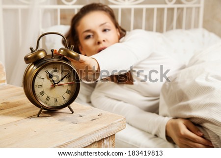 Young woman in bed turning off alarm clock