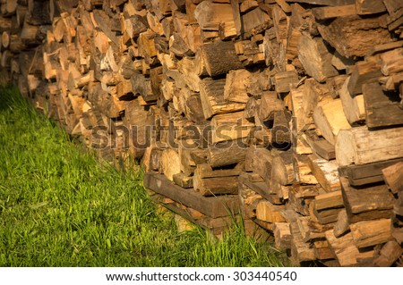 Picturesque old yellow billets stacked high logstack wall loaded on green grass lit by bright evening summer warm sun. View close-up with space for text on garden lawn