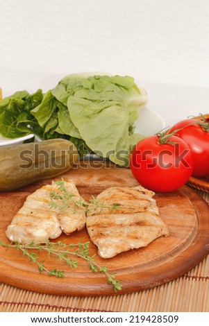 Grilled chicken with tomatoes and gherkins on a wooden cutting board