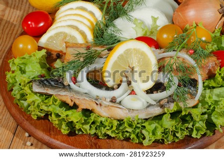 Smoked mackerel fillet with salad, lemon, onions, tomato, garnished with dill on a wooden kitchen board