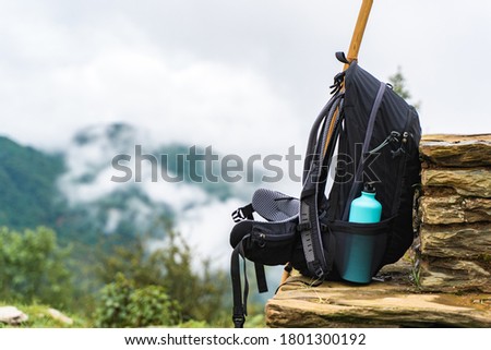 Backpack with water bottle and bamboo stick on stone fence near chasm. Mountains are hidden by clouds. Hiking and trekking concept. Imagine de stoc © 