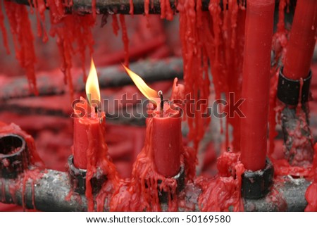 Many red candles with wax dripping in a Buddhist shrine in China.  Two of the candles have flames.