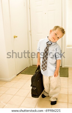 A cute young boy is dressed as a businessman, and stands by the door, carrying a briefcase