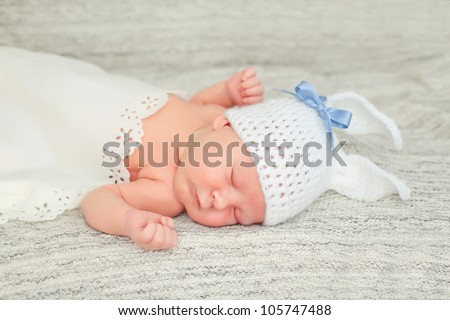 A newborn baby is wearing a white funny rabbit hat and laying down sleeping on a soft white background. Soft focus, shallow DoF.