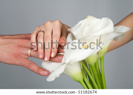Groom and bride holding hands to reveal rings while displaying the flowers.