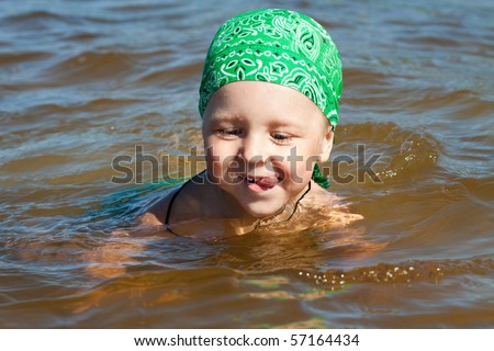 young boy in turquoise sea, learning to swim with green bandana, smiling happy