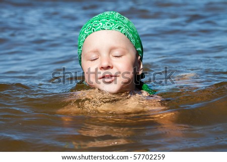 young boy in turquoise sea, learning to swim with green bandana, smiling happy
