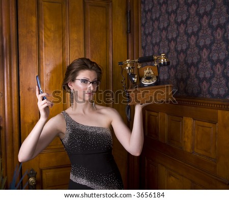 Beautiful young brunette woman wearing an evening gown holding an old fashioned telephone in one hand and a modern cell phone in the other. See my portfolio for more like this.