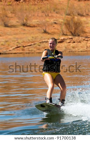 Girl wakeboarder enjoying water sports boarding behind a boat with beautiful Lake Powell in  the background at Glen Canyon National  Recreation Area, Utah, USA
