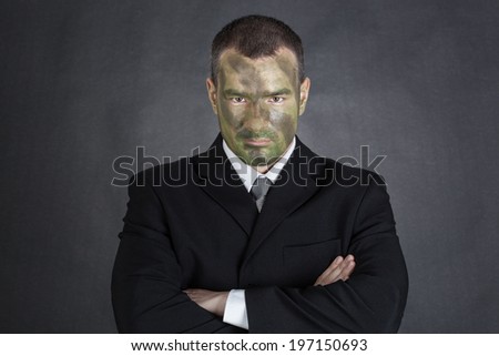 Serious businessman with jungle camouflage paint and crossed arms on black background