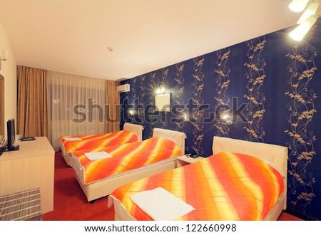 Interior of a hotel room for three persons, blue wallpapers and orange sheets on beds.