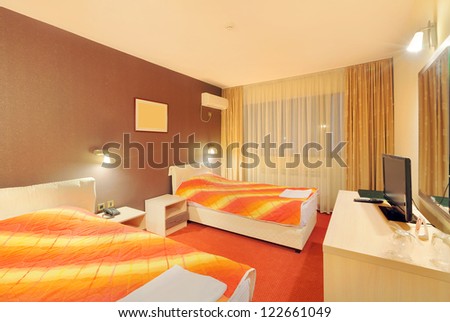 Interior of a hotel room for two, with furniture. Orange and brown colors as a main design details.
