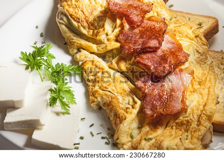 Breakfast meal, scrambled eggs and bacon served on white plate.