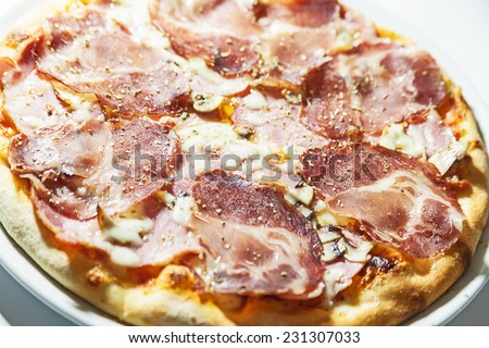 Pizza with meat and ham, served on white plate.