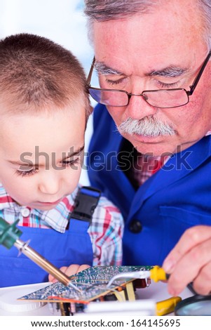 Grandfather teaching grandchild working with soldering iron