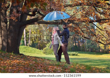 Couple in love with blue umbrella resting in autumn forest