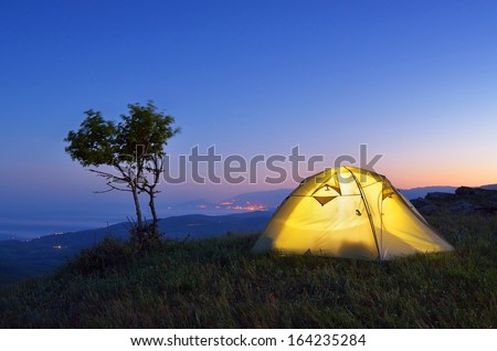Night landscape with a tent in the mountains. The light from the lantern in a tent. Camping in the countryside. Crimea, Ukraine, Europe