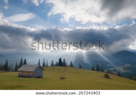 Rural landscape with beautiful sun rays through the clouds. Wooden hut in the mountains