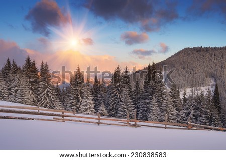 Winter landscape in the mountains. Sunny morning with beautiful clouds. Wooden fence on a mountain meadow in the forest. Christmas landscape