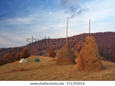 Tourist camping in the mountain village. Autumn landscape. Haystacks on the meadow