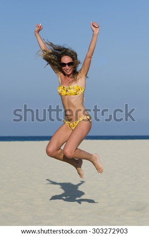 Smiling girl jumps up on the sand with her arms up and legs raised