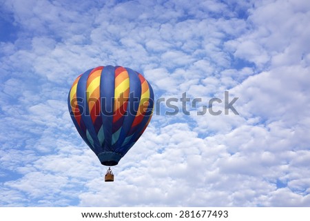Single hot air balloon floating up into a blue sky full of white fluffy clouds