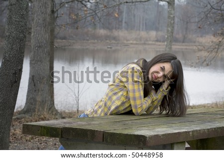 Beautiful brunette woman in front of lake propped on picnic table