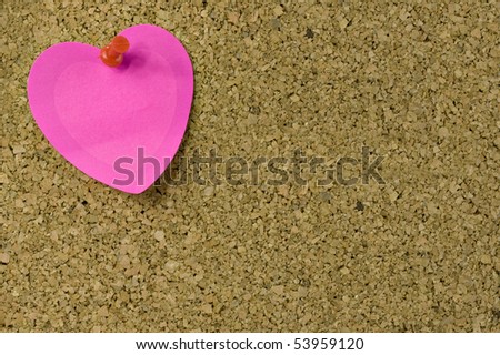 Pink heart shaped note on with red thumb tack on bulletin board