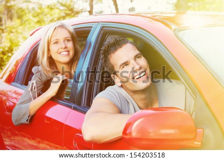 Two young smiling people in a red car