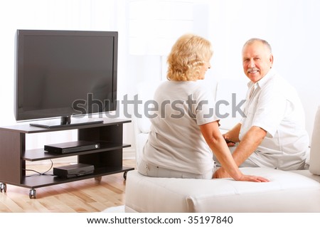 Happy smiling elderly couple watching TV at home