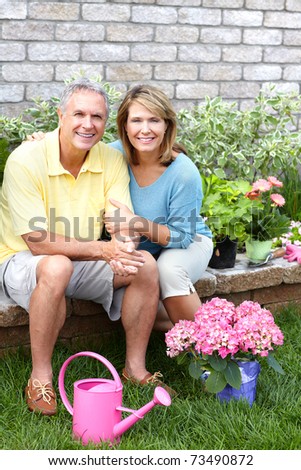 Smiling happy elderly seniors couple gardening near the home