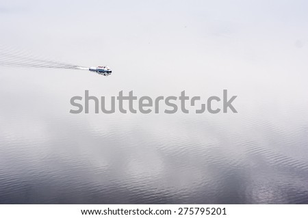Pleasure boat on the vast expanse of water. Clouds are reflected in water