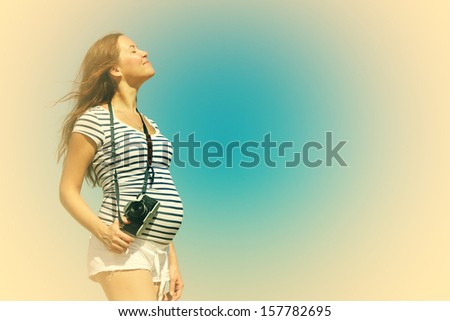 Young pregnant woman holding vintage camera. Photo in old color image style.