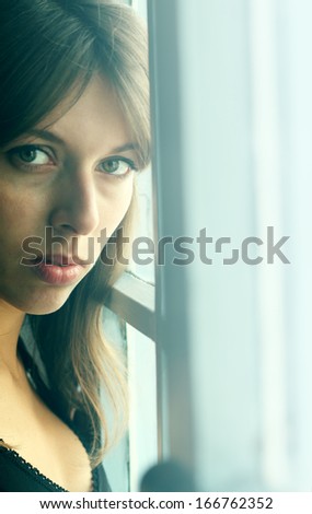 Art portrait of a beautiful young sadly girl looking through the window