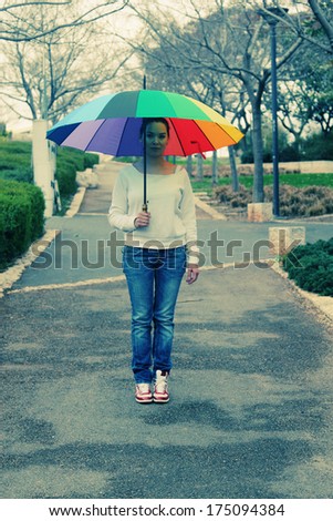 Young woman standing under a big rainbow umbrella