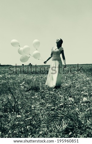 Young woman holding pink balloons and walking in a meadow. Photo in old color image style.