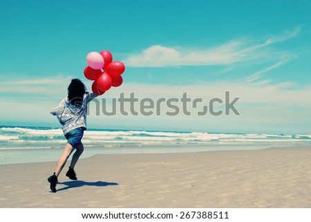 beautiful woman holding red balloons and walking on seaside