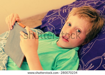 7 year old boy lies in bed and plays with a laptop