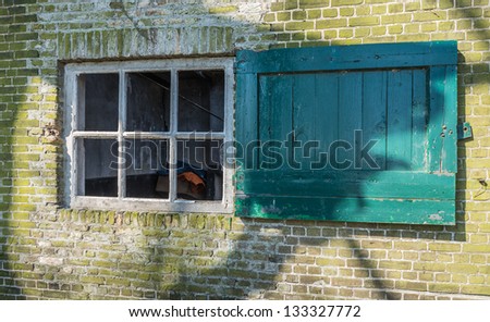 Brick facade with an old white window and a green painted window shutter.