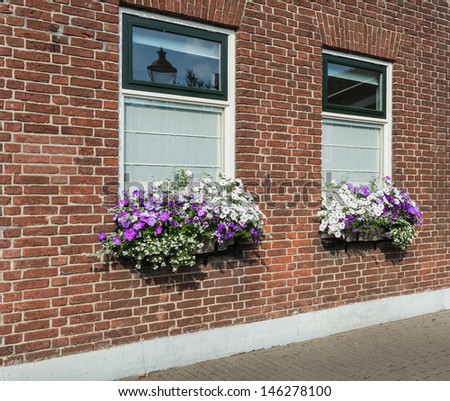 Closeup of a masonry brick wall with windows and flower boxes with colorful blooming plants.