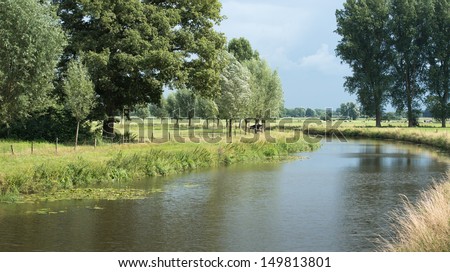 Rural area in the Netherlands with rain clouds, a narrow curved river and grazing cows in the distance.
