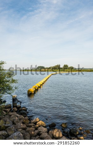 Wide creek in a Dutch nature reserve closed with a barrier of floating switched yellow plastic objects