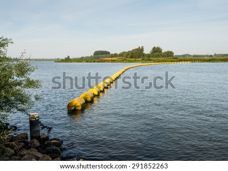 Wide creek in a Dutch nature reserve closed with a barrier of floating switched yellow plastic objects